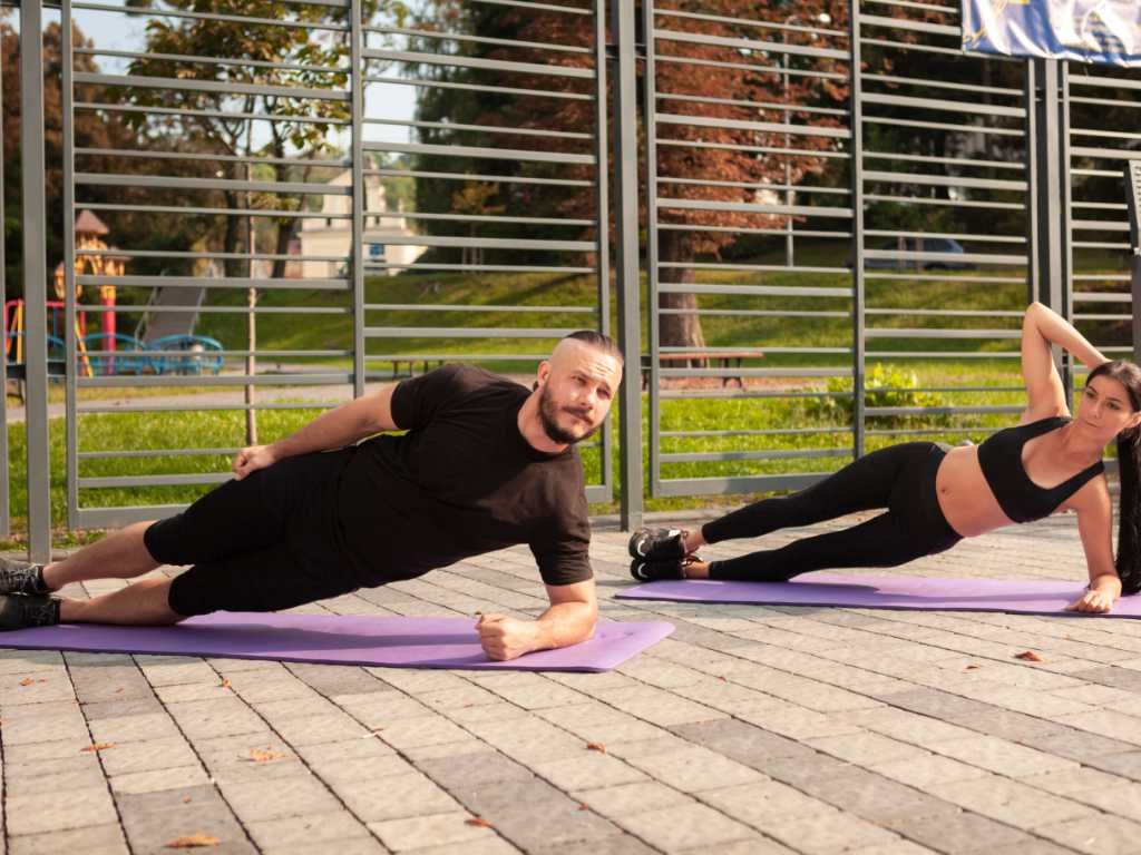 Couple performing side plank exercises for core strength demonstrating proper lateral stability form outdoors