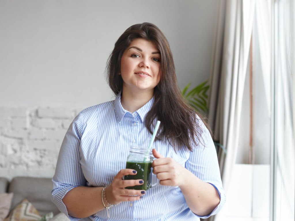 Professional woman holding green meal replacement shakes in office setting for weight management and nutrition