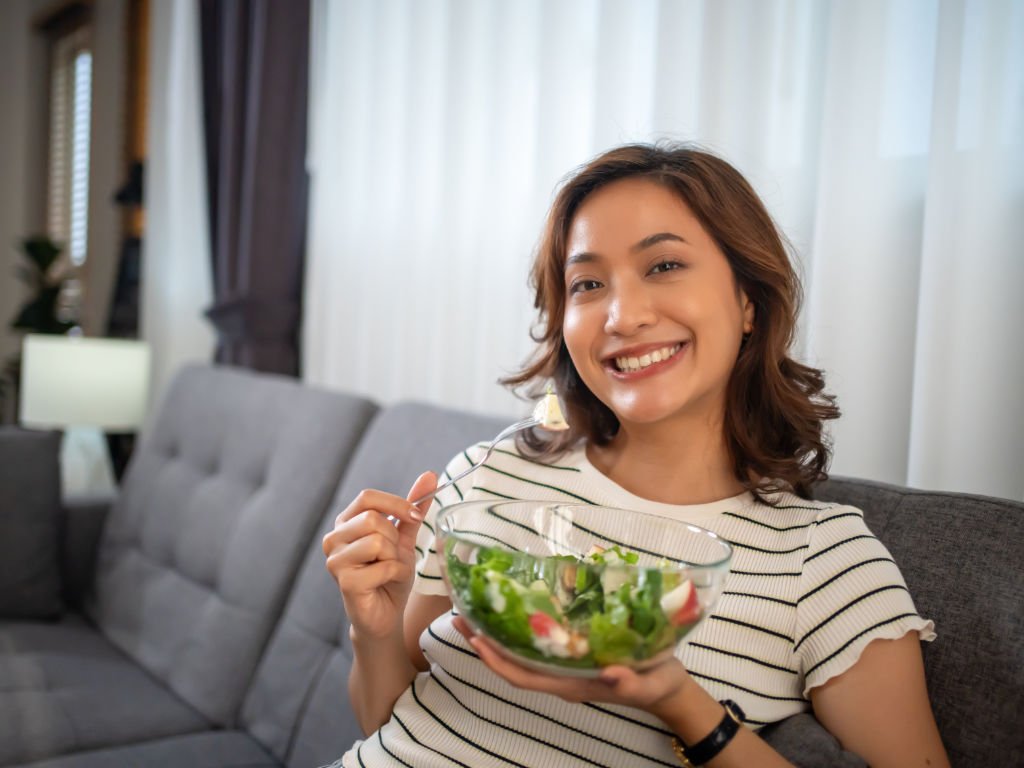 Happy woman eating fresh green salad with superfoods demonstrating optimal daily nutrition timing at home