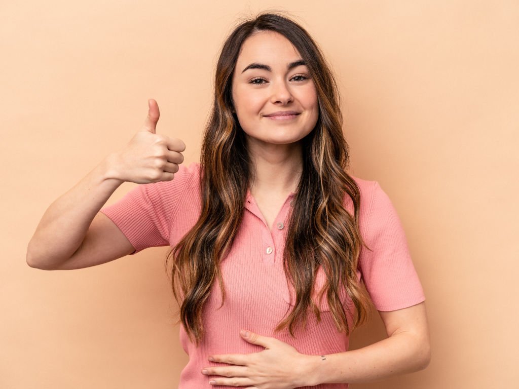 Happy woman giving thumbs up while touching stomach showing benefits of probiotic supplements for digestive health