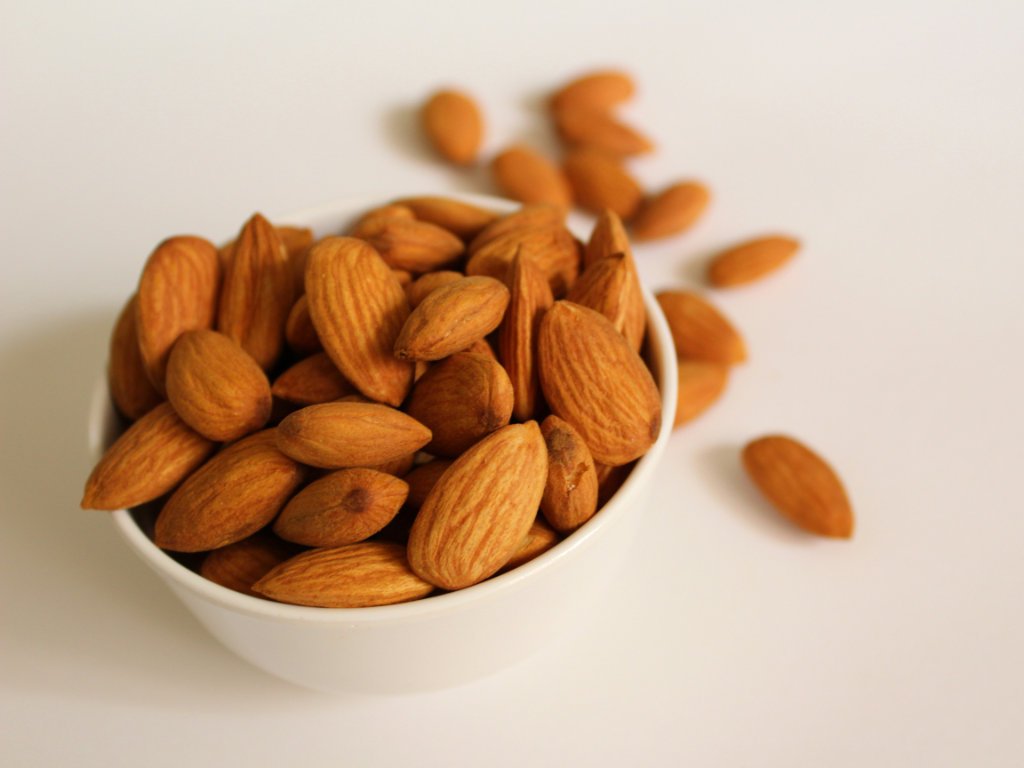 Raw almonds superfoods for immunity rich in vitamin E for cellular protection in white bowl on clean background
