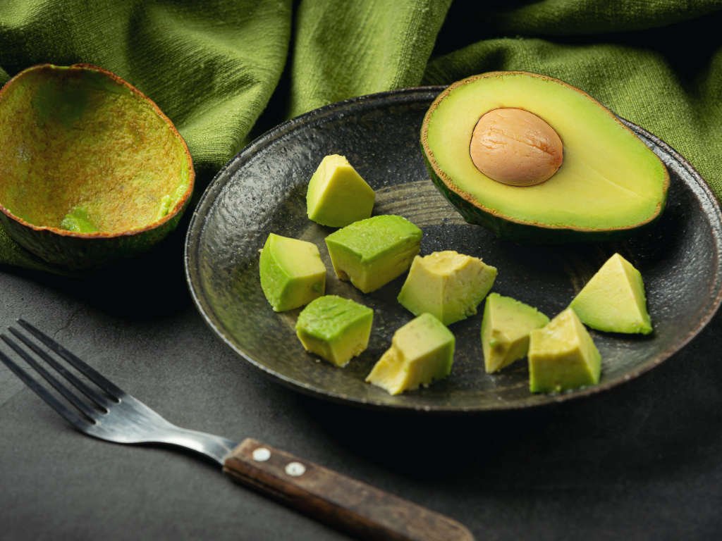 Cubed avocado pieces on black plate with fork and avocado halves, superfoods for metabolism support