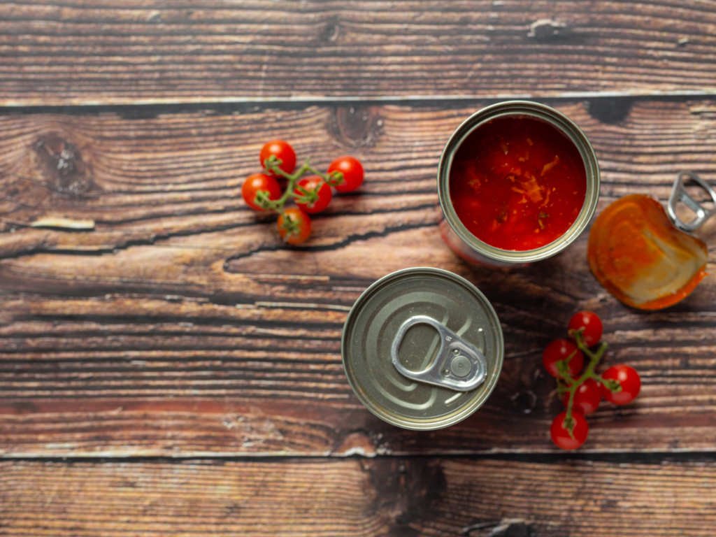 Opened can of tomato sauce staple foods with fresh cherry tomatoes on wooden surface for flavor enhancement in healthy meal preparation