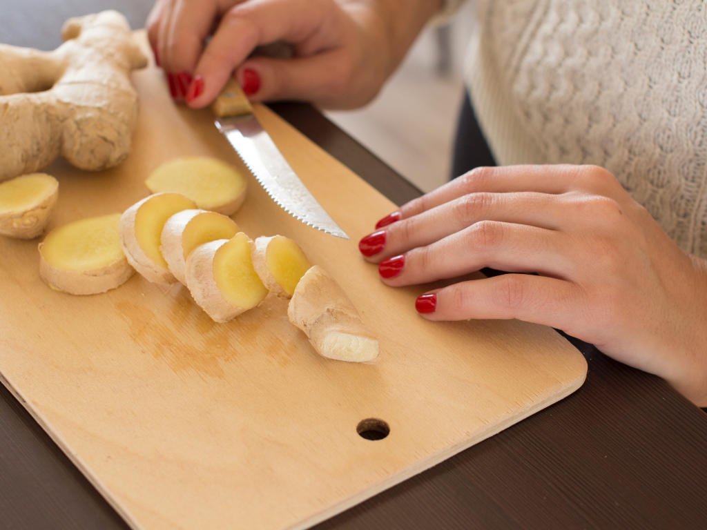 Hands slicing fresh ginger root on cutting board demonstrating how to prepare natural ingredients for weight loss strategy