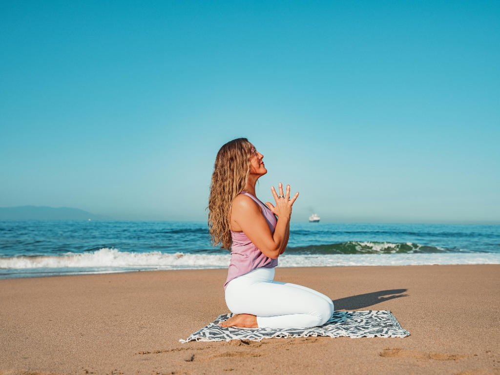 Woman practicing daily emotional wellness techniques through beach meditation and mindful breathing exercises on yoga mat