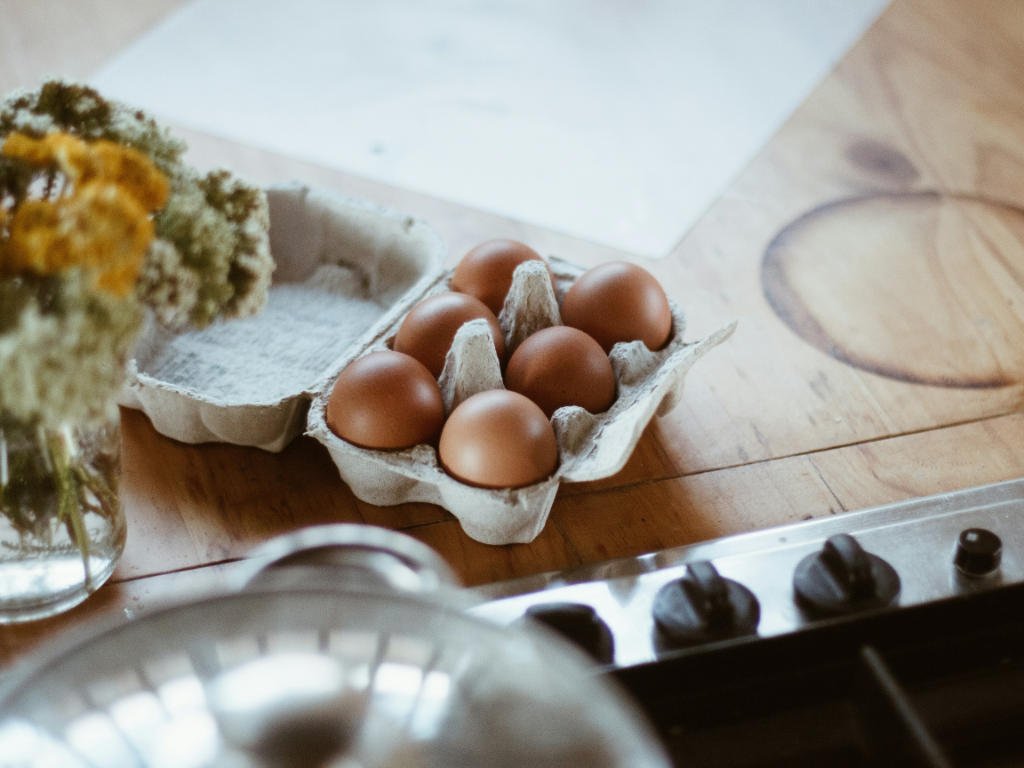 Fresh eggs in carton on kitchen counter with cooking supplies - versatile protein staple foods for healthy meal preparation