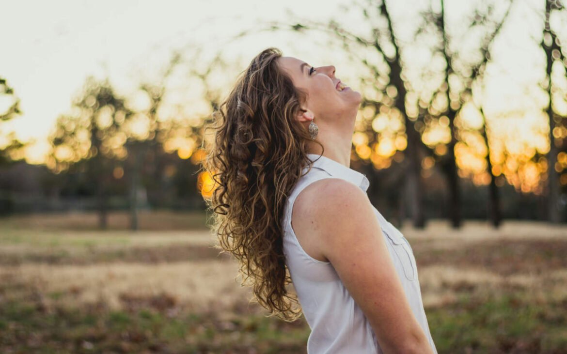 oyful woman practicing emotional wellness techniques outdoors, demonstrating the positive effects of daily mental health practices in natural sunlight