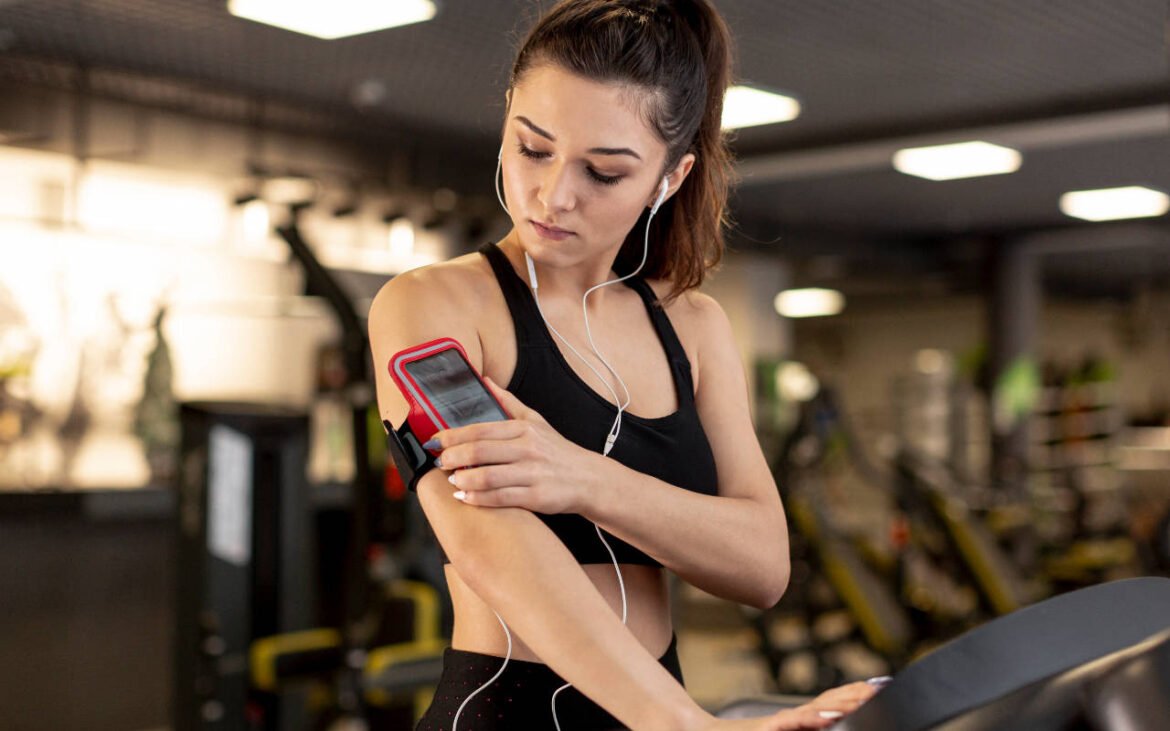 Woman using fitness gadgets for women including smartphone armband and earphones during gym workout session