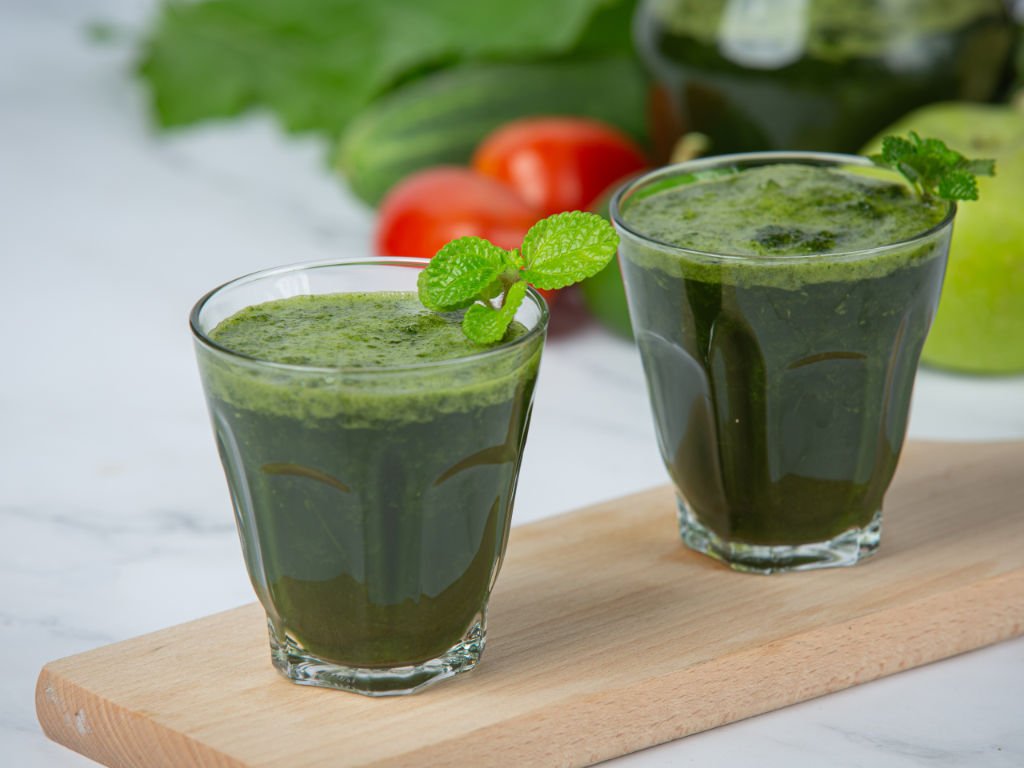 Two green smoothies with mint garnish on wooden board - liquid antioxidant snacks packed with nutrients for active individuals