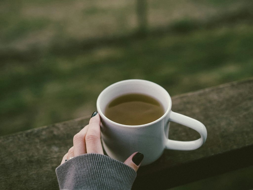 Hand holding white mug of green tea outdoors showcasing natural ingredients for weight loss benefits