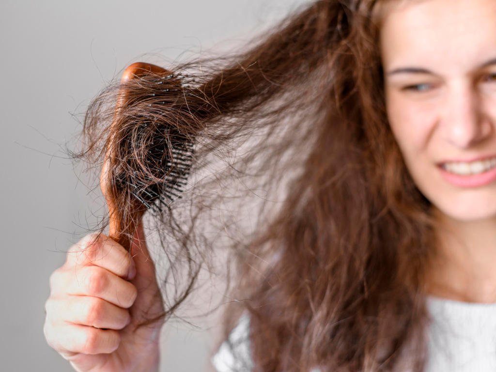 Woman brushing tangled hair showing daily damage that hair oil for women helps prevent and protect against