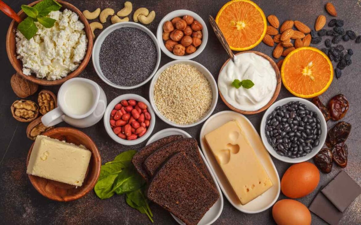 Variety of nutritious staple foods including cottage cheese, chia seeds, quinoa, black beans, nuts, yogurt, cheese, and eggs arranged on dark surface for healthy meal preparation