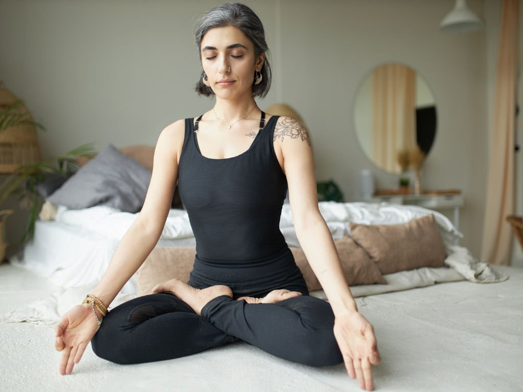 Woman practicing mindful yoga for mental health in peaceful home setting with eyes closed in lotus meditation pose