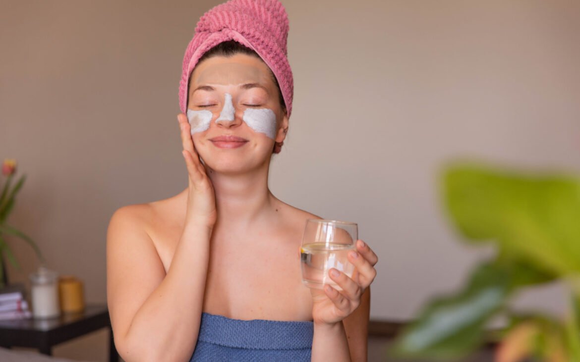 Woman practicing hydration techniques for skin health while drinking water and wearing hydrating eye patches during skincare routine