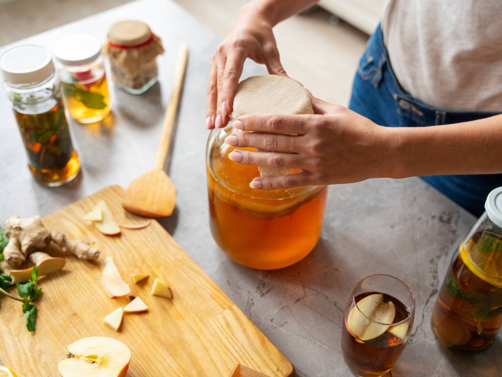 Person brewing homemade kombucha, a trendy newcomer among probiotic-rich foods, covering fermentation jar with cloth