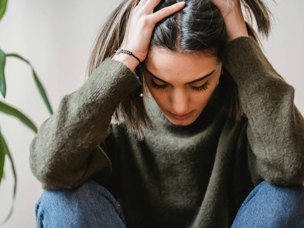 Woman experiencing headache from magnesium insufficiency holding her head in discomfort at home