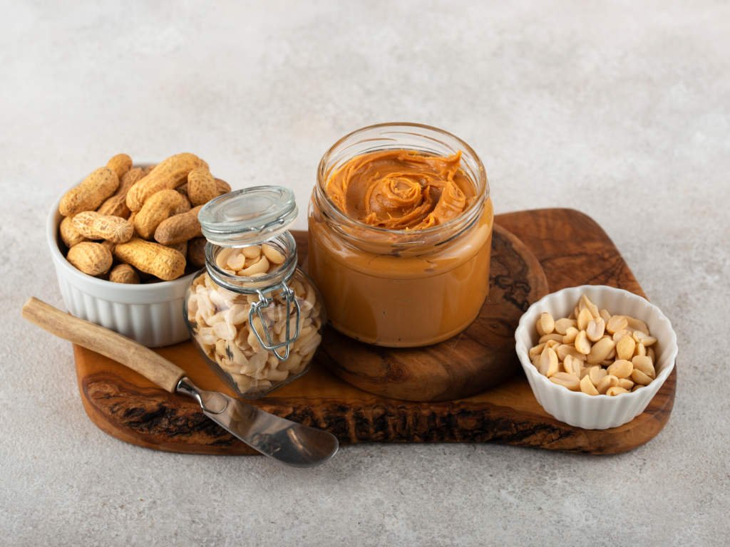 Peanut butter jar with whole peanuts and nuts on wooden board - satisfying staple foods for healthy meal preparation