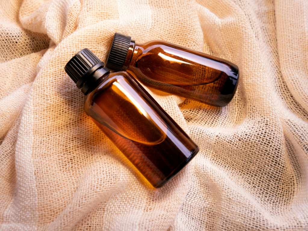 Two amber glass bottles of organic hair oil for women displayed on natural burlap fabric representing clean beauty products