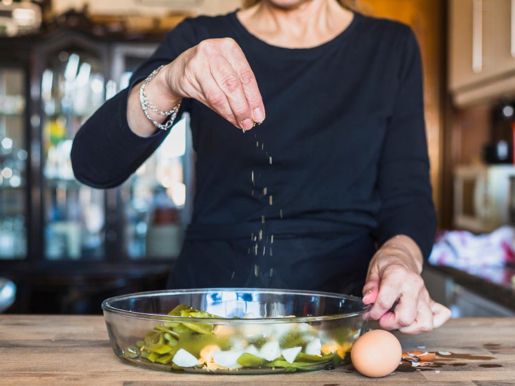 Woman seasoning fresh salad in kitchen demonstrating real-world application of natural ingredients for weight loss in meal planning