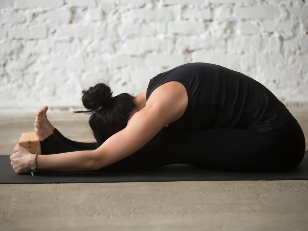 Woman performing Seated Forward Bend (Paschimottanasana) yoga for mental health and stress relief on black yoga mat