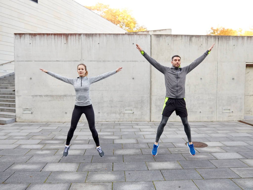 Two fitness enthusiasts demonstrating smart cardio workouts integration with synchronized jumping jacks exercise