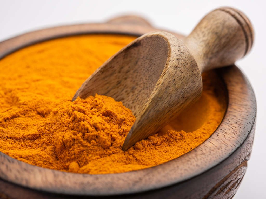 Golden turmeric powder in wooden mortar and pestle representing powerful metabolism boosting spices for weight loss and anti-inflammatory benefits