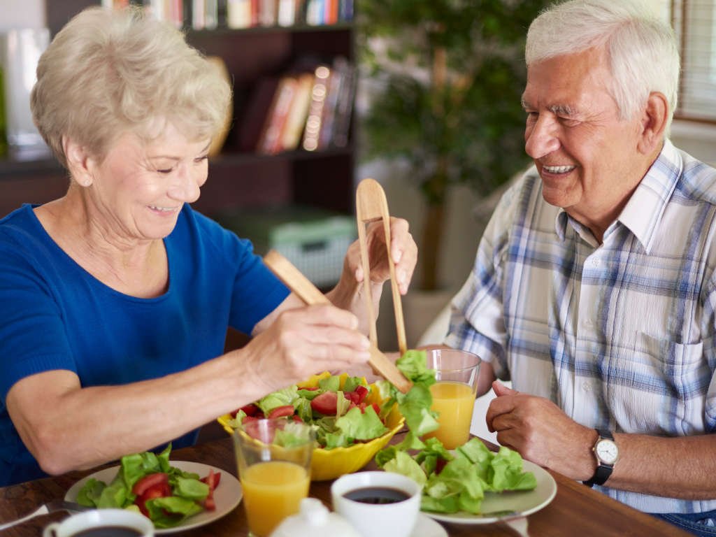Happy senior couple eating fresh salad showing how older adults need adequate vitamin B intake for healthy aging