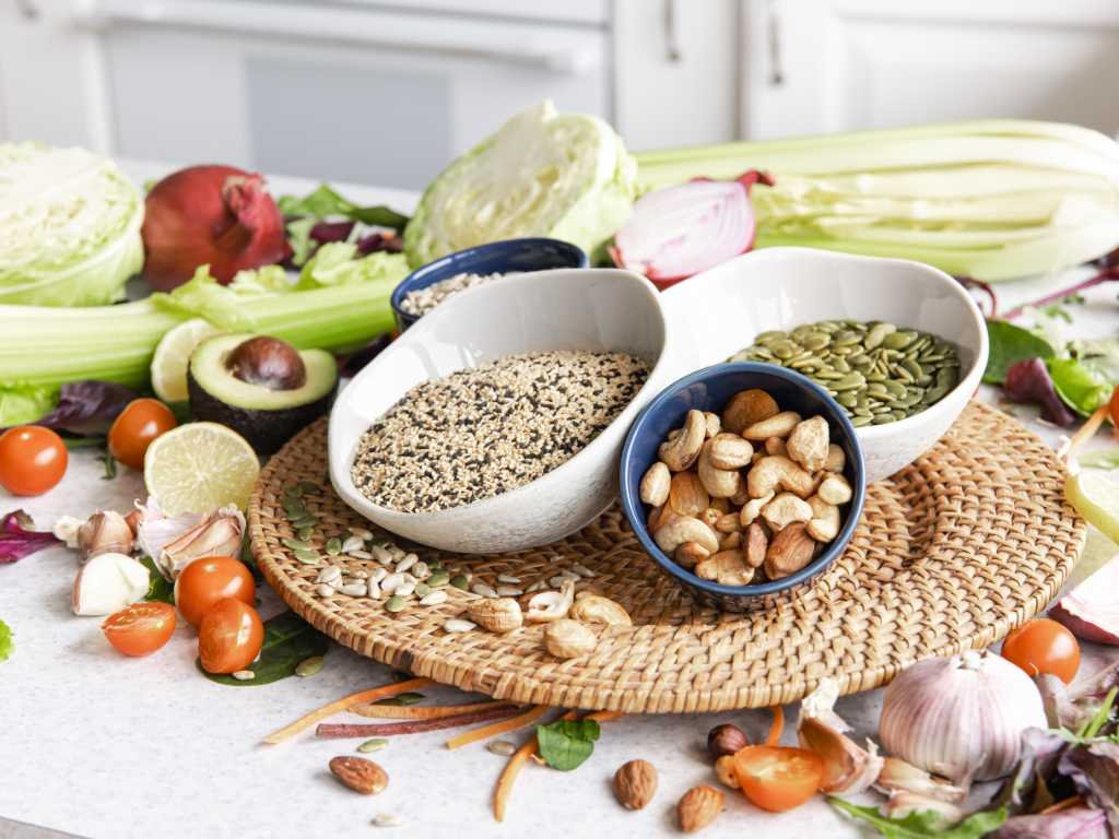 Variety of plant-based vitamin B sources including leafy greens, nuts, seeds, and vegetables arranged on kitchen counter