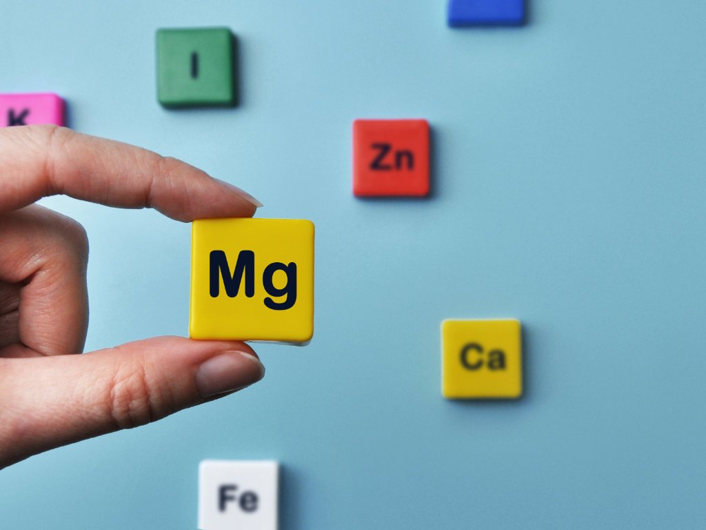 Hand holding magnesium element block with other essential minerals showing different magnesium for headaches supplement options