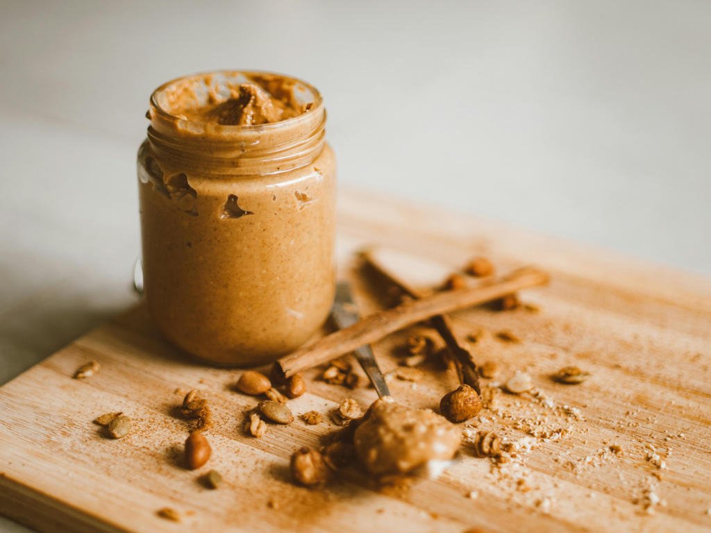 Jar of creamy peanut butter with nuts and ingredients for no-bake homemade protein bars