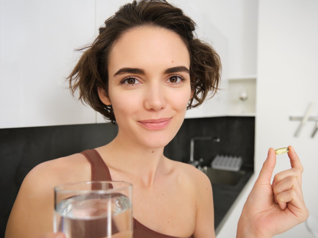 Woman holding vitamin K2 supplement capsule with glass of water demonstrating proper supplementation